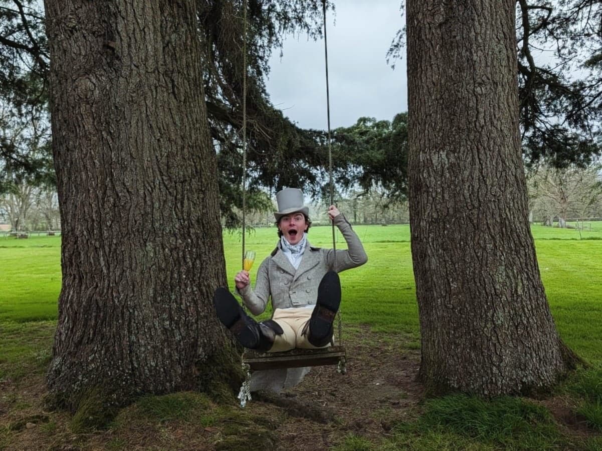 A costumed figure swings between two old trees on the manor lawn.